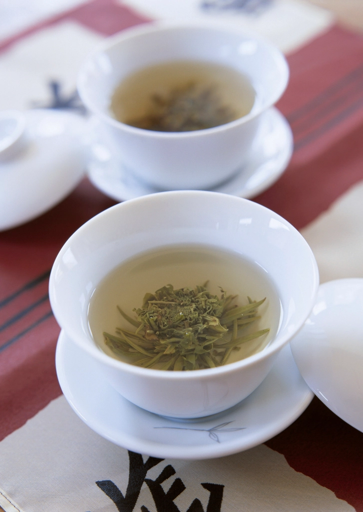 白磁の蓋碗にひらいた煎茶の茶葉と、淡く澄んだ水色（すいしょく）